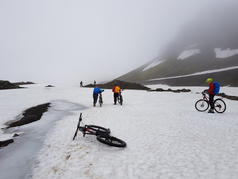 The group going across a snowfield with their mountain bikes. 