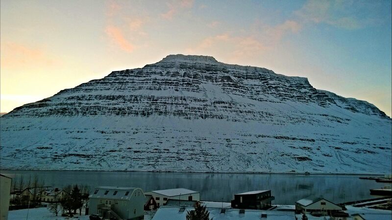 The mountain Hólmatindur in Eskifjörður. There is snow in the mountain and faint light behind it. 
