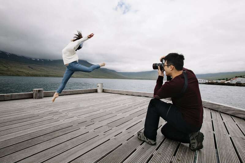 On the pier in Fáskrúðsfjörður. A man is taking a picture of woman on the pier who is dancing. 