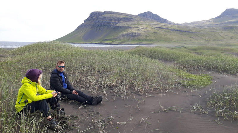 A man and woman are taking a rest sitting in the sand in Vöðlavík. 