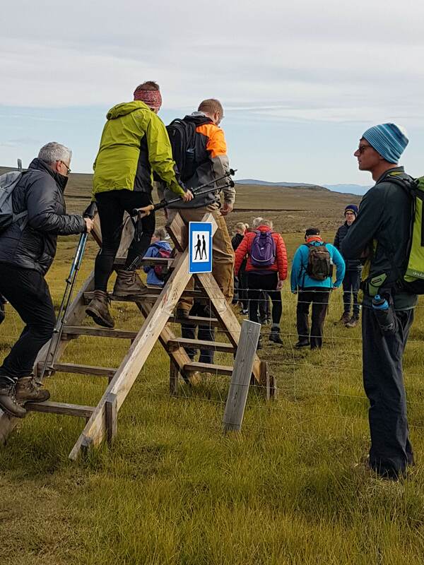 Skúli wilderness guide with a group of hikers going over a walking bridge over a fence. 