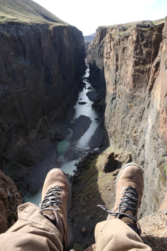 A photo taken overlooking Hafrahvammagljúfur and the shoes of the traveler are in the forefront of the picture. 